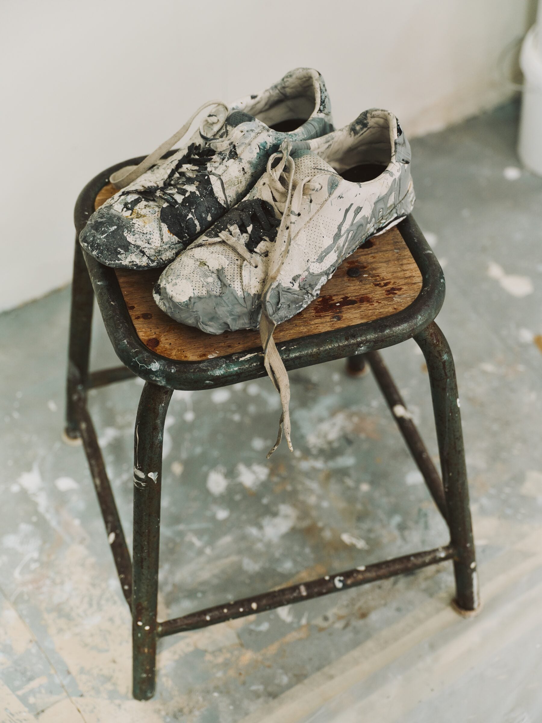 Farbbespritzte Sneaker auf einem Atelierhocker